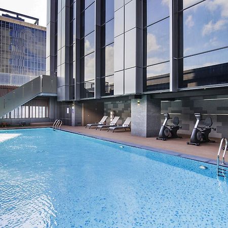 臺北 台北凯达大饭店酒店 外观 照片 The photo shows a modern outdoor swimming pool surrounded by a sleek, contemporary building. The pool has a clear blue surface and is bordered by a wooden deck. There are a few lounge chairs placed around the pool for relaxation. In addition, some ex