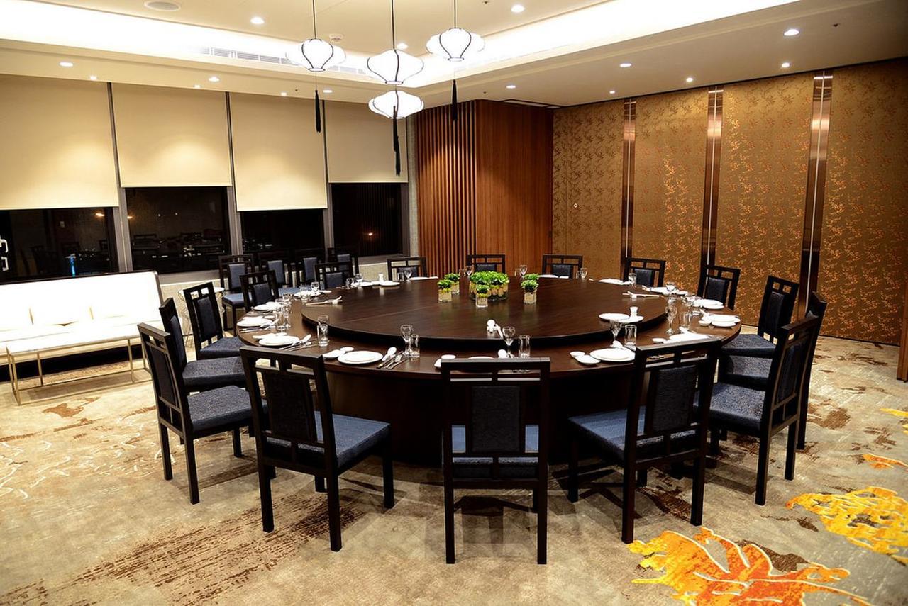 臺北 台北凯达大饭店酒店 外观 照片 The photo shows a large, elegantly set dining room with a circular table surrounded by black chairs. The table is equipped with plates, utensils, and glassware, suggesting it's prepared for a formal meal. The room features modern lighting fixtures ha