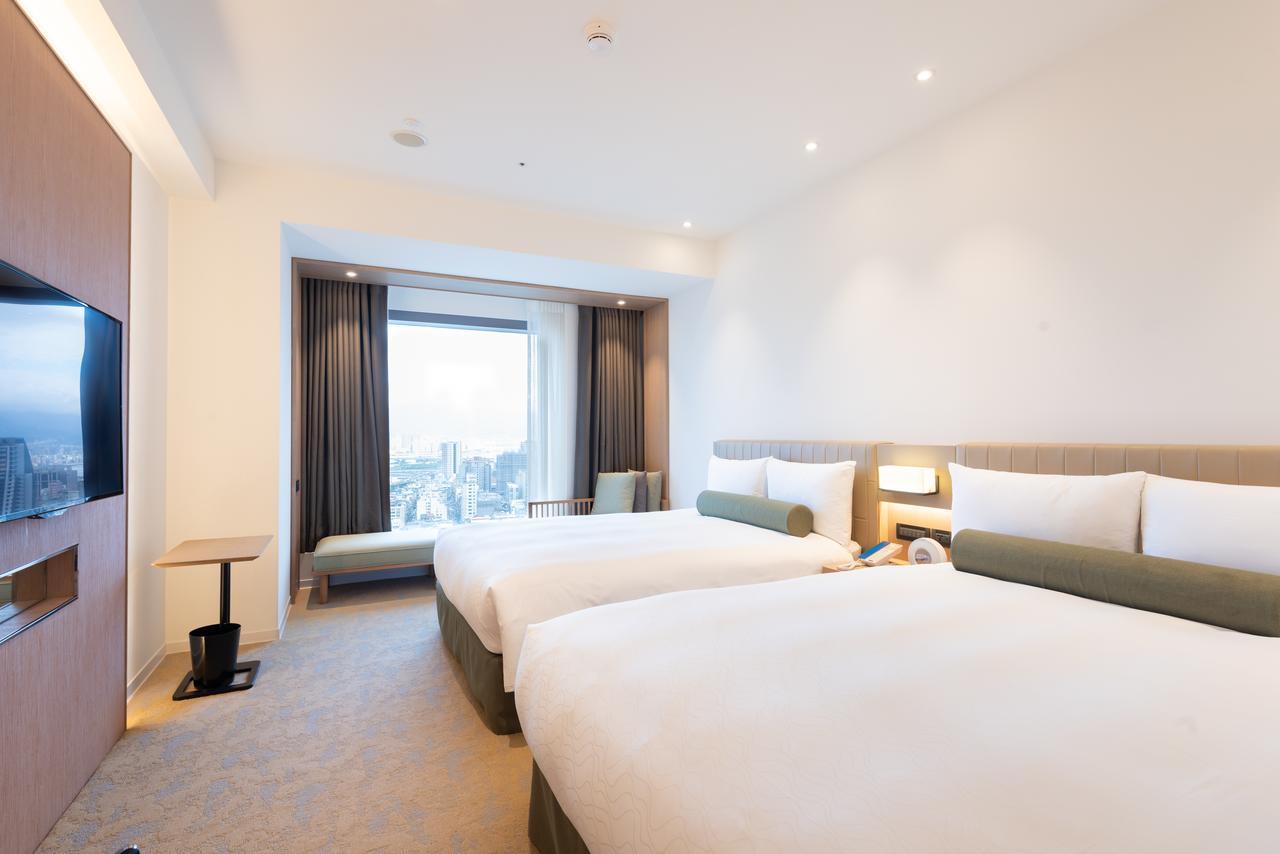 臺北 台北凯达大饭店酒店 外观 照片 The photo shows a modern hotel room featuring two twin beds with white bedding and green accent pillows. The walls are painted in light colors, creating a spacious and bright atmosphere. A large window allows natural light to enter, offering a view o