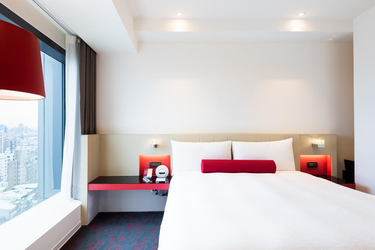 臺北 台北凯达大饭店酒店 外观 照片 The photo shows a modern hotel room featuring a large bed with white bedding and two pillows. There is a decorative red bolster pillow on the bed. The room has minimalist decor with a light-colored wall and a stylish design. On either side of the bed