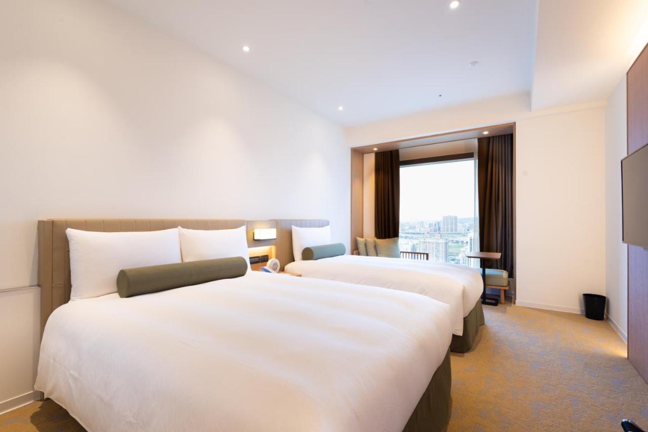 臺北 台北凯达大饭店酒店 外观 照片 The photo shows a modern hotel room with two beds. Each bed has crisp white linens and a decorative gray bolster pillow. The room features a minimalist design with light-colored walls and a neutral carpet. There’s a large window with curtains that pa