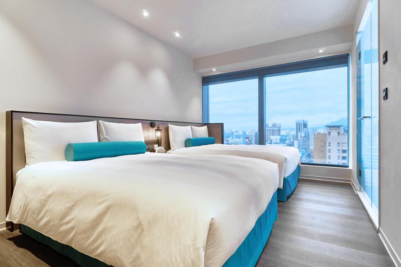 臺北 台北凯达大饭店酒店 外观 照片 The photo depicts a modern hotel room featuring two beds. The beds have white bedding and turquoise accent pillows. Large windows allow natural light to enter, providing a view of the city outside. The room has a contemporary design, with a clean and