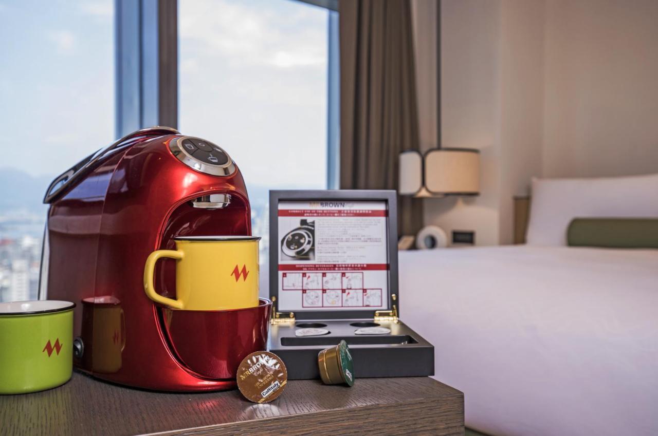 臺北 台北凯达大饭店酒店 外观 照片 The image shows a cozy hotel room setting featuring a red coffee maker on a wooden table. Next to the coffee maker are two yellow mugs and a brown capsule, likely used for coffee. There is also a box containing a selection of coffee capsules. In the 