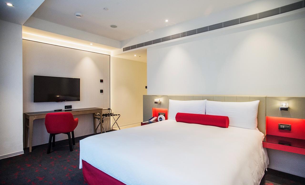 臺北 台北凯达大饭店酒店 外观 照片 The photo shows a modern hotel room. It features a large bed with white bedding and a red accent pillow. There is a desk area with a chair, a small table, and a flat-screen television mounted on the wall. The room has a bright and minimalist design, 