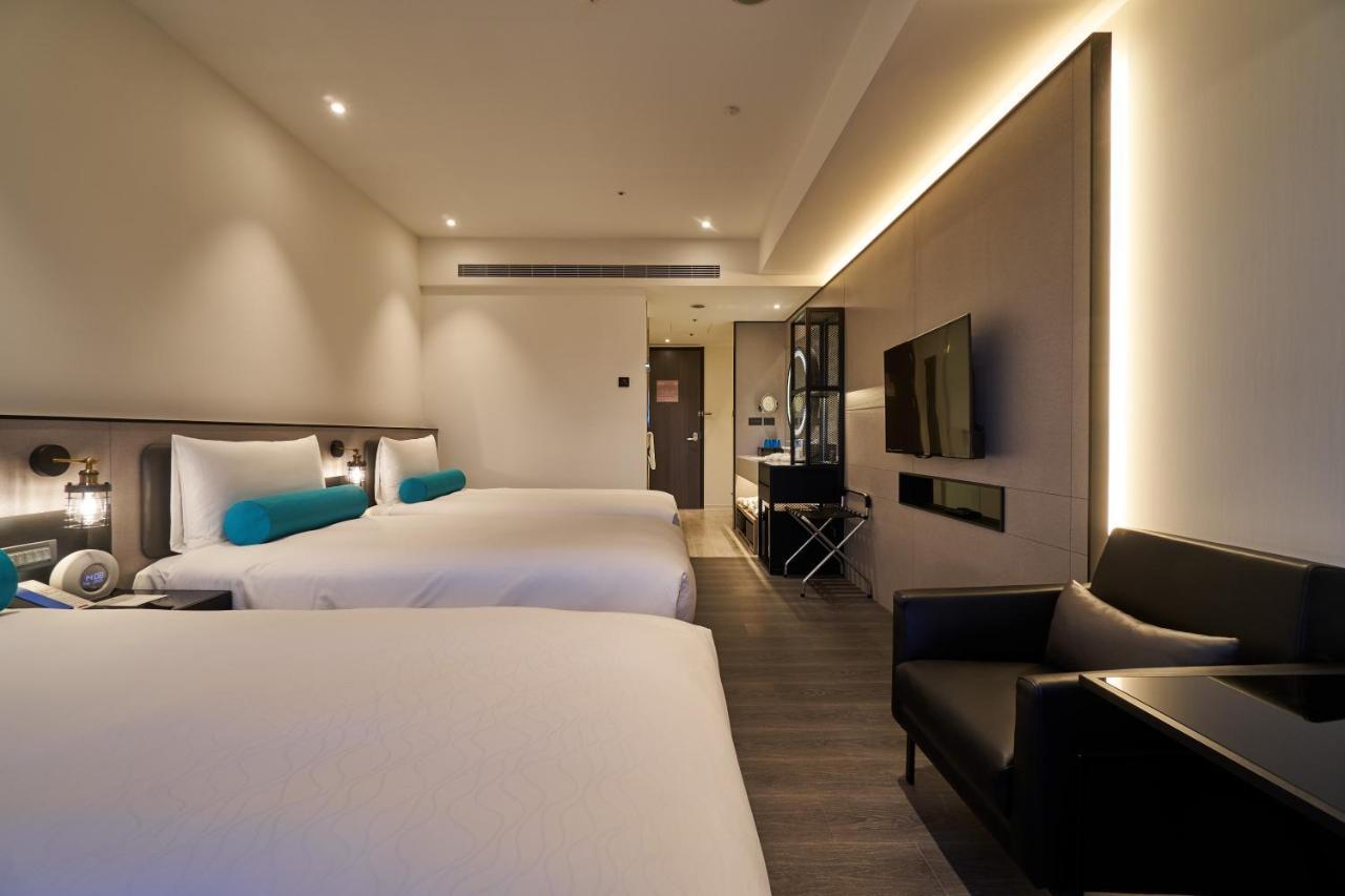 臺北 台北凯达大饭店酒店 外观 照片 The photo displays a modern hotel room featuring two beds with white linens and turquoise accent pillows. There's a sleek black chair positioned next to one of the beds. A flat-screen TV is mounted on the wall opposite the beds, and there's a stylish