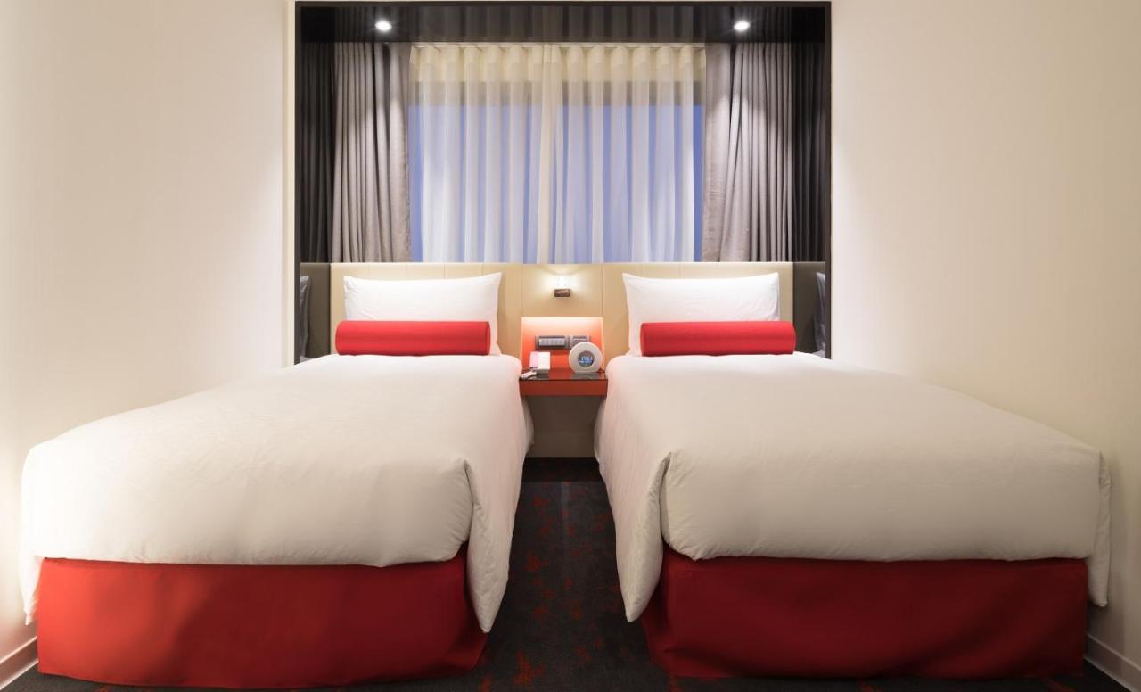 臺北 台北凯达大饭店酒店 外观 照片 The photo shows a hotel room featuring two beds. Each bed has a white comforter with a red accent at the bottom. There are decorative red pillows on top of the beds. The room is bright, with sunlight filtering through sheer curtains, and the walls ar