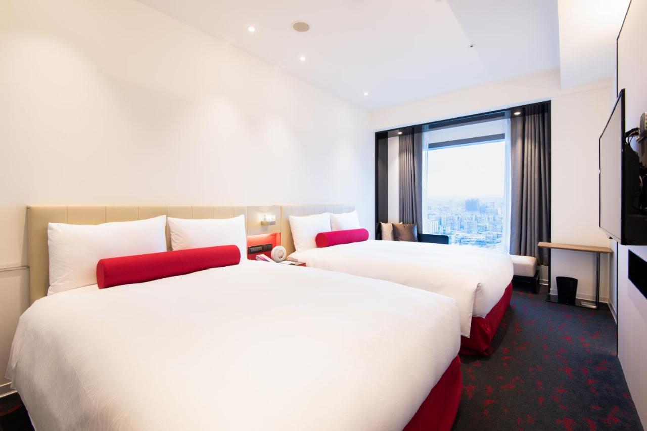 臺北 台北凯达大饭店酒店 外观 照片 The image shows a modern hotel room featuring two queen-sized beds with white bedding and red accents. The room is spacious with neutral-colored walls, and there is a large window that provides natural light and a view. On one side, there's a small d