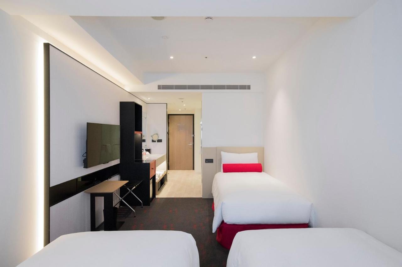 臺北 台北凯达大饭店酒店 外观 照片 The photo shows a modern hotel room featuring three beds. The beds are neatly made with white linens and some have red accents. On one side of the room, there is a flat-screen television mounted on the wall and a small table with chairs. The decor is