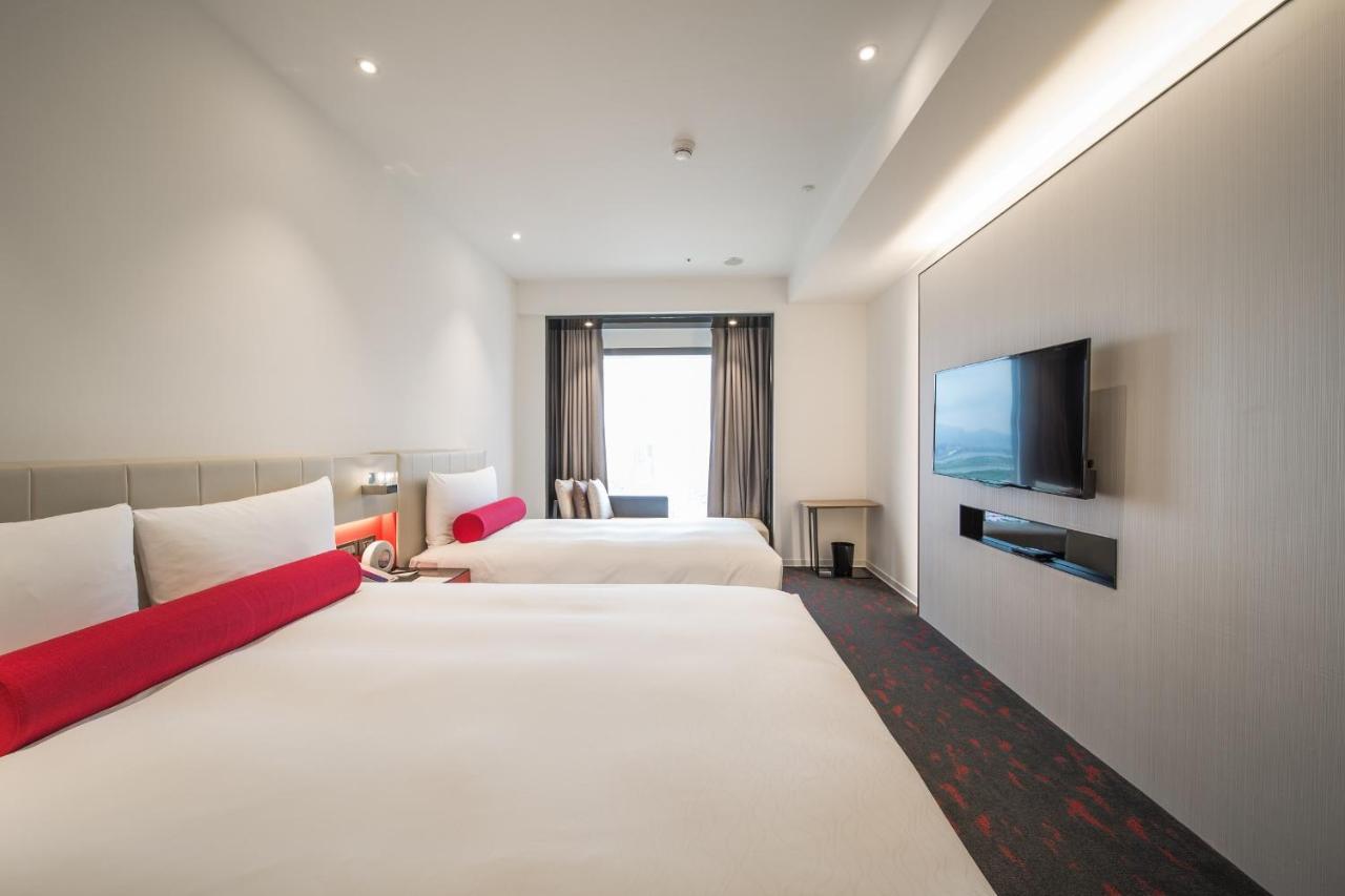 臺北 台北凯达大饭店酒店 外观 照片 The photo shows a modern hotel room featuring two large beds with white linens and red accent pillows. There is a window with curtains that allow natural light to enter the room. On the wall opposite the beds, there is a flat-screen television mounte