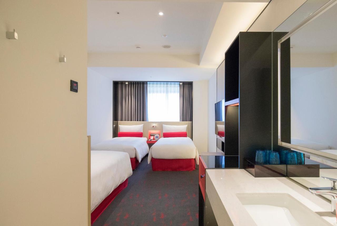 臺北 台北凯达大饭店酒店 外观 照片 The photo shows the interior of a hotel room. It features two single beds with white linens and red accents. There is a window with sheer curtains allowing natural light to enter the room. The floor is carpeted, and the decor is modern and minimalist